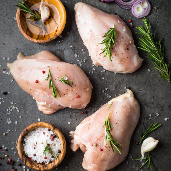 Raw chicken breasts with herbs and spices on a dark surface